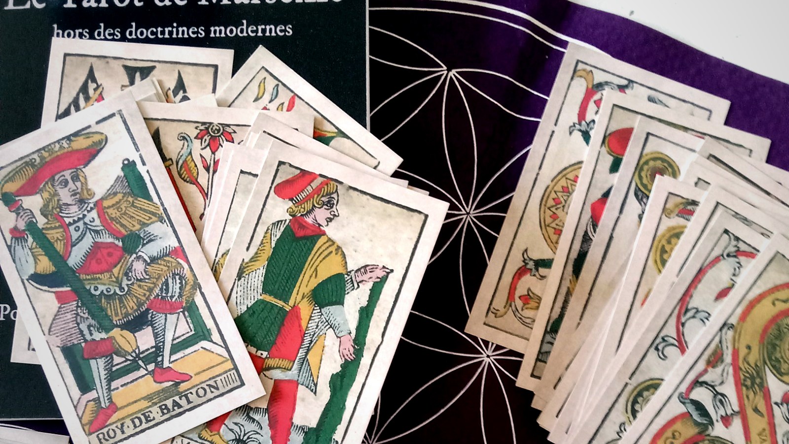 Cartes de couleurs du Tarot de Marseille disposées autour du livre Élucider le Tarot de Marseille de Daminus